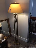 Full view of the 61 inch tall floor lamp with beige shade and metal crisscross base on wooden floor.