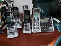 Five Panasonic cordless phone handsets and one base station displayed on a table, all in black with silver details.