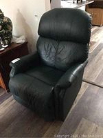 Front angled view of green leather recliner rocking chair showing padded armrests and cushioned backrest.