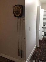 Full view of German pendulum wall clock mounted on wall, showing wooden case, three weights hanging from chains, and pendulum setup.