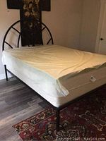 Full view of queen bed with metal headboard, mattress, box spring, and memory foam topper covered in protective plastic.