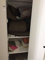 Closed cabinet shelf showing brown comforter with animal print pillows on top and folded sheets below