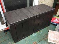 Front angled view of rectangular brown resin outdoor storage bin showing panel details and wood grain texture.