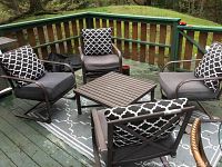 Set of four patio chairs with cushions and pillows arranged around square metal table on a painted wooden deck outside.