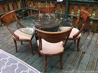Full view of glass top round table with four wooden chairs on outdoor deck