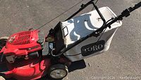 Full side view of a red Toro 4-cycle self-propelled lawn mower with white grass collection bag attached to rear.