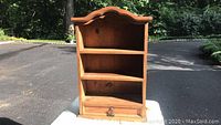 Front view of pine wall cabinet showing two shelves and curved top edge.