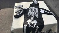 Black skeleton costume jumpsuit laid out on table with matching hood and gloves