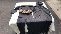 Two-piece Batman Halloween costume laid out on a table showing the muscle suit with belt and separate black cape with hood and mask.