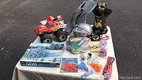 Photo showing the red monster truck toy, knight helmets, shield, puzzle box, and various small toys and trinkets displayed on a table outdoors.
