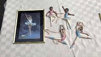 Framed ballerina print and five ballerina figurines laid out on light checkered fabric background.
