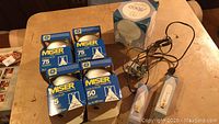 4 boxes of GE Miser 75W floodlight bulbs, 1 box of GE Miser 50W floodlight bulb, GE LED A19 bulb box, and 2 clear filament bulbs attached to wires on a table.