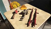 Full view of the lot of old tools arranged on a beige table including a hand drill, mounting plate, crank drill, and pipe clamps