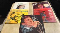 Five vinyl LP records displayed showing album covers of classic country music artists including Hank Williams, Waylon Jennings, Johnny Cash, and Bob Seher.