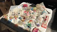 Wide view of crafting materials laid out on a white tablecloth, showing various bags of beads, hooks, metal rings, scissors, and threads.