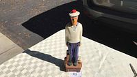 Front view of ceramic sailor figurine on table outdoors with car in background.