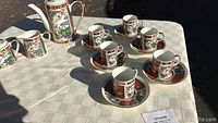Photo of the coffee set on a table outdoors showing coffee pot, creamer, sugar bowl, six cups and saucers all with detailed floral design