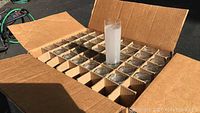 Open cardboard box showing 40 individual frosted glasses packed in compartments, one glass filled with water for scale