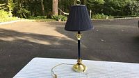 Navy blue lamp displayed on a white surface outdoors, sunlight casting shadow, showing the lamp and its shade