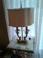 Pair of brass table lamps on a small table next to window showcasing lamp shape, size and fabric shades.