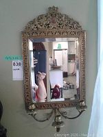 Full view of antique brass wall candelabra with beveled edge mirror showing ornate detailed frame and reflective glass.