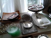 Overview of various platters, trays, plates including glass green plates, metal serving trays, and a covered glass dish