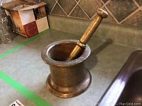 Brass mortar with pestle inside on a kitchen counter, showing wear and patina.