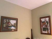 Wide angle view showing both fabric needlework art pictures hanging on adjacent walls, framed and displayed.