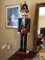 Full front view of the 36-inch wooden nutcracker, showing the detailed painted uniform and facial features, against a background with framed artwork and a mirror.