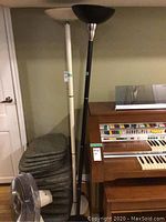 Photo showing two floor lamps side by side, white and black, with a stack of chair pads behind and a Sears floor fan in front.