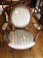 Front view of one Louis XVI armchair showing oval backrest, carved pecan wood frame, and light brocade upholstery with visible damage.