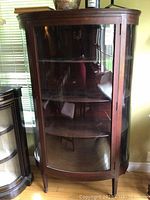 Front view showing curved glass door, interior shelves, and tapered legs on casters