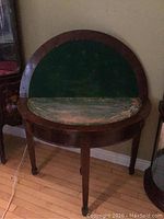 Photo showing the demi lune table closed with flip-top raised revealing worn green felt.