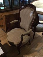 Photo showing the full antique parlour chair with carved wood frame, beige brocade upholstery, armrests, and casters on the legs.