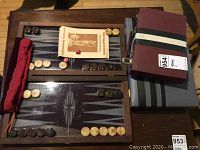 Backgammon game set displayed with playing pieces arranged on the board, red dice, instruction booklet, cloth pouch, and carrying cases visible.