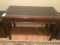Full view of rectangular wood desk with black glass insert on top, showing the single front drawer with two knobs and dark brown finish.