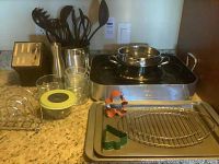 All kitchen items displayed on a kitchen counter including roasting pan, baking sheets, pie plate, cutlery, cookie cutters, wire rack, knives, and utensils