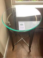 Side angled view of round glass topped side table with metal legs and crossbar support.
