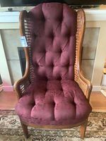 Front view of wing back chair showing tufted burgundy fabric seat and backrest with rattan sides and wooden legs.