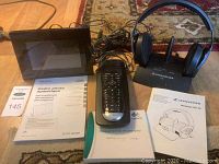 Overview of all items including Sennheiser headphones on charging base, Logitech Harmony One remote with manual, and Sony digital photo frame with instructions.