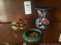 Photo of the three Moorcroft ceramic items together on wood surface, showing the covered dish, small dish, and vase with floral patterns.