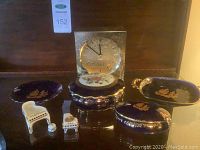 Overall view of Limoges trinket boxes, dishes, miniature pianos, and Seiko mantel clock grouped together on wood surface.