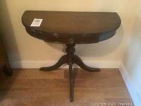 Front view of the wood half circle side table showing the drawer and tripod base.