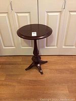 Full view of the round wooden pedestal table in front of closed doors on hardwood flooring.