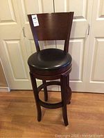 Front view of wooden swivel bar stool with black upholstered round seat and backrest