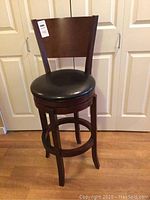 Full view of dark wooden swivel bar stool with padded black seat and backrest against a door background.