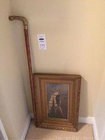 Framed art print with walking stick leaning against wall.