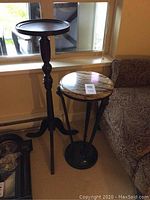 Full view of both plant stands side by side by a window and couch, showing the wooden pedestal and metal marble stands.