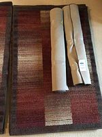 Overview of one area rug with two rolled-up rugs on top showing the surface and design.