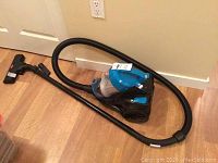 Full view of Bissell PowerForce vacuum cleaner with hose and extended wand on wooden floor.